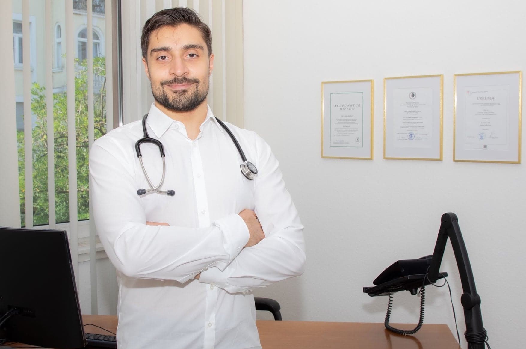 Dr. med. A. Haidary in seinem Sprechzimmer, im Hintergrund seine Facharzt- und Akupunktur-Urkunden